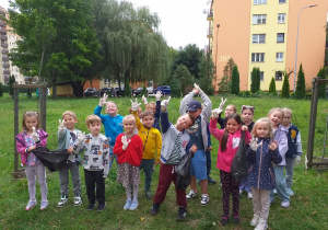 Zdjęcie przedstawia dzieci z grupy Odkrywcy przygotowane do akcji „Sprzątanie Świata” na trawniku w pobliżu przedszkola.