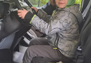 Chłopiec siedzi za kierownicą radiowozu straży miejskiej i z uśmiechem udaje kierowcę.