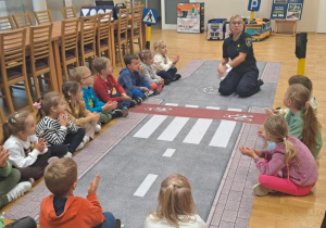 Dzieci siedzą w kręgu i słuchają pani podczas zajęć o bezpieczeństwie na drodze.