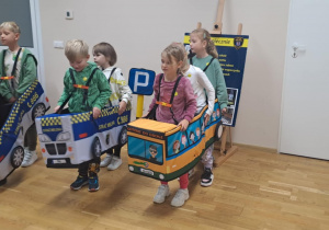 Dzieci stoją w autochodzikach, biorąc udział w zabawie edukacyjnej o bezpieczeństwie na drodze.