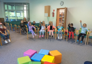 Zdjęcie przedstawia dzieci zgłaszające się do udzielenia odpowiedzi na pytanie pani bibliotekarki.