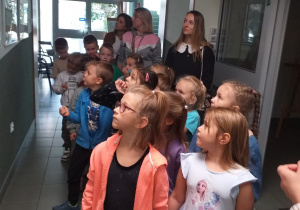 Zdjęcie przedstawia dzieci słuchające zasad przebywania w bibliotece.