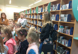 Zdjęcie przedstawia dzieci słuchające sposobów poszukiwania książek za pomocą katalogu w komputerze.