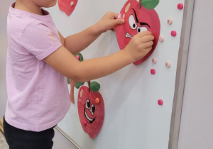 Chłopiec przyczepia na tablicę wydrukowane jabłko.