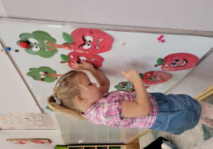 Dziewczynka przyczepia na tablicę wydrukowane jabłko.