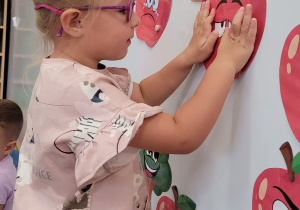 Dziewczynka przyczepia na tablicę wydrukowane jabłko.