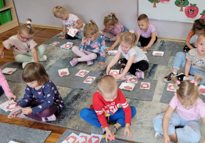 Dzieci z grupy Słoneczka siedzą na dywanie i dopasowują kształty.