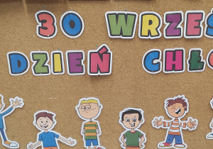 na zdjęciu przedstawiona jest przyczepiona na tablicę dekoracja z okazji dnia chłopaka. Napis: 30 września dzień chłopaka oraz wycięte, kolorowe postaci dzieci.