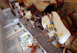 na zdjęciu widzimy dzieci siedzące przy stolikach i częstujące się smakołykami rozłożonymi na kolorowych talerzykach.