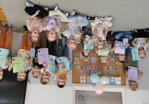 zdjęcie przedstawia uśmiechnięte dziewczynki i chłopców pozujących na tle dekoracji. Chłopcy trzymają w dłoniach dyplomy oraz otrzymane upominki. Dziewczynki także trzymają w dłoniach prezenty.