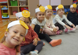 Dzieci z grupy Biedronki siedzą na dywanie z opaskami uśmiechniętych buziek.