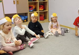 Przedszkolaki siedzące na dywanie z opaskami na głowie w kształcie buziek.