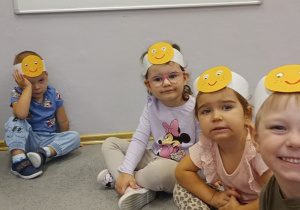 Przedszkolaki z grupy Biedronki siedzą na dywanie a na głowie mają opaski z buziami.