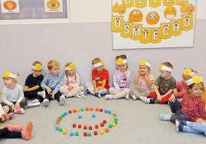 Dzieci siedzą na dywanie dookoła buzi ułożonej z klocków.