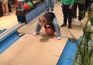 Dziewczynka turla kulę reszta dzieci czeka w kolejce.