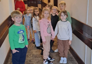 Grupa dzieci stoi na korytarzu w hotelu, pod opieką nauczyciela w tle.