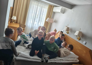 Dzieci wygłupiają się na łóżku w pokoju hotelowym.