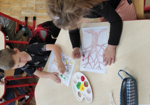 dzieci siedzące przy stoliku tworzą kolorowe liście na pracy plastycznej przy użyciu farby i patyczków higienicznych.