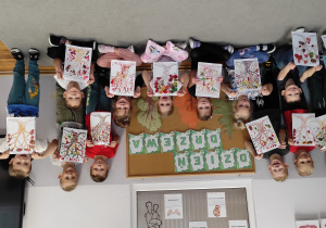 11 uśmiechnięte przedszkolaki na tle dekoracji prezentują wykonaną przez siebie pracę z okazji dnia drzewa.