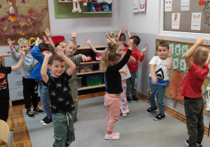 na zdjęciu uśmiechnięte dzieci z rękoma uniesionymi do góry udają, że są szumiącymi drzewami.