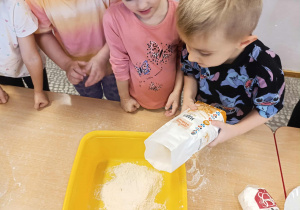 Chłopiec wsypuje mąkę do miski.