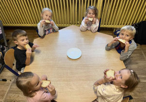 Dzieci siedzą przy stolikach, zajadają się świeżo upieczonym chlebem.