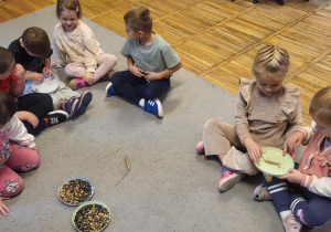 Dzieci siedzą na dywanie, obierają kłos żyta.