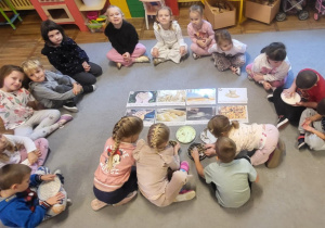 Dzieci siedzą na dywanie, oglądają różne rodzaje zboża i mąki.