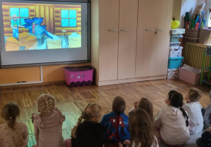 Dzieci oglądają filmik edukacyjny na tablicy multimedialnej ,,Od ziarenka do bochenka”.