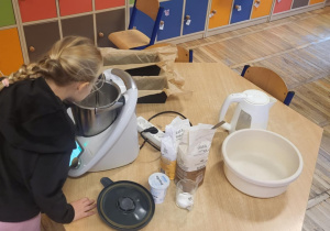 Dziewczynka zagląda do kielicha urządzenia wielofunkcyjnego Thermomix, aby zobaczyć co stało się z drożdżami.