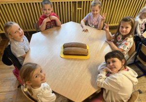 Dzieci siedzą przy stolikach z upieczonym chlebem.