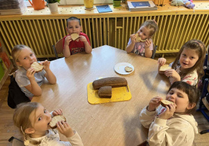 Dzieci siedzą przy stolikach, zajadają się świeżo upieczonym chlebem.