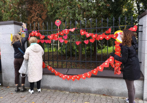 Panie wieszają łańcuch serc na płocie.