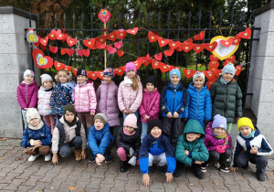 Dzieci z grupy Motylki pozują do zdjęcia na tle łańcuchów z serduszek.