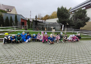 Dzieci z grupy Motylki pozują do zdjęcia, za nimi są lamy.