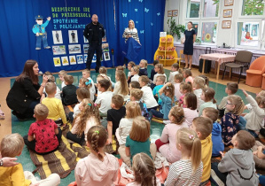 Na zdjęciu widzimy Panią Policjantkę, która zadaje dzieciom pytania na temat numeru alarmowego.