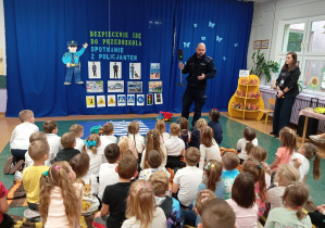 Na zdjęciu widzimy Policjanta demonstrującego sygnalizator świetlny przy przejściu dla pieszych.