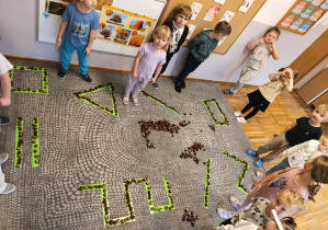 Dzieci układają z kasztanów wzory na dywanie na wyklejonych taśmami paskach.
