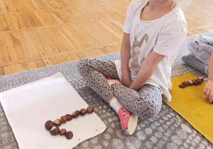 Dziewczynka ułożyła z kasztanów na dywaniku cyfrę 1.