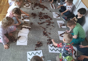 Dzieci układają z kasztanów różne wzory na przygotowanych szablonach.