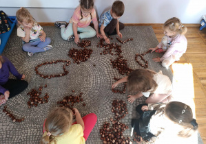 Dzieci sierdzą na dywanie i układają z kasztanów różne wzory.