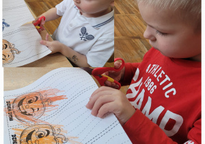 Dwaj chłopcy siedzą przy stoliku i wycinają.