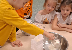 Chłopiec wsypuje mąkę do miski reszta dzieci przygląda się.