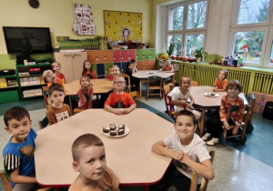 Dzieci siedzą przy stolikach na stole leżą babeczki dyniowe.