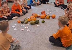 Dzieci siedzą w kole na dywanie na środku leżą dynie i zadania matematyczne.