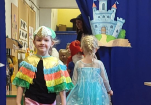 Dziewczynka przebrana za papugę idzie po czerwonym dywanie w bajkowym pokazie mody.