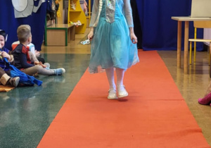 Dziewczynka przebrana za Elzę idzie po czerwonym dywanie w bajkowym pokazie mody.