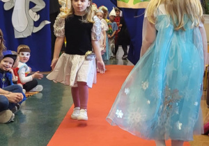 Dziewczynka przebrana za wróżkę idzie po czerwonym dywanie w bajkowym pokazie mody.