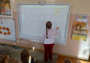 Zdjęcie przedstawia dziewczynkę przy tablicy interaktywnej która gra w Dyniowe memory