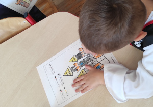 Chłopiec siedzący przy stoliku koloruje ilustrację bajkowego zamku.